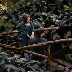 Blog - Woman Smiling While a Man is Down on One Knee and They are on a Trail in the Woods